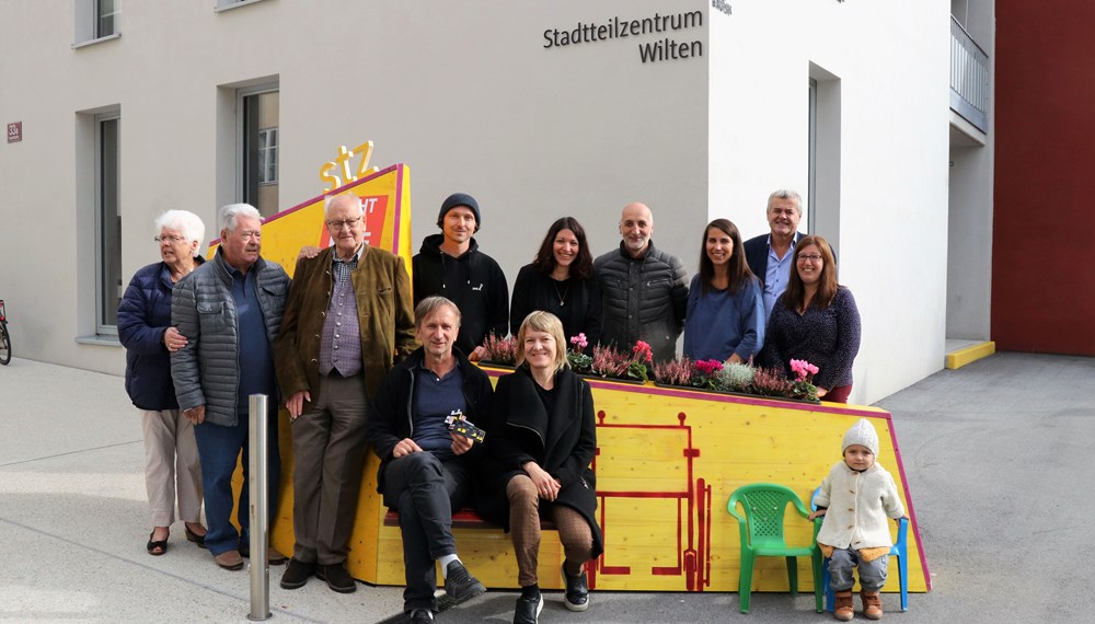 Kreativ, bunt und unübersehbar – so präsentiert sich seit 4. Oktober das temporäre, öffentliche Möbelstück vor dem Stadtteilzentrum Wilten in der Leopoldstraße 33a. Die Idee für das hölzerne Bauwerk entstand im Rahmen eines Beteiligungsprozesses bereits im Dezember 2017. Damals kamen NachbarInnen, ein Kreativteam aus Wilten und VertreterInnen des Stadtteilzentrums zusammen, um über die Gestaltung des Innenhofes zu beratschlagen. Die nun realisierte Konstruktion enthält die gewünschten Elemente, bestehend aus Beschriftung, Informations- und Plakatflächen, einem Buchtauschregal, Sitzgelegenheiten und kann mit Blumentöpfen ausgestattet werden. Bei der Einweihung kamen viele Beteiligte und UnterstützerInnen zusammen, unter ihnen auch Gemeinderätin Janine Bex, Geschäftsführer Hubert Innerebner (Innsbrucker Sozialen Dienste, ISD), Stadtteilkoordinatorin Florence Fritz sowie das Kreativteam rund um Charly Walter und zahlreiche AnrainerInnen. Bis Juni 2021 lädt das öffentliche Möbelstück vor dem Stadtteilzentrum Wilten zum Verweilen und Verwenden ein. AA