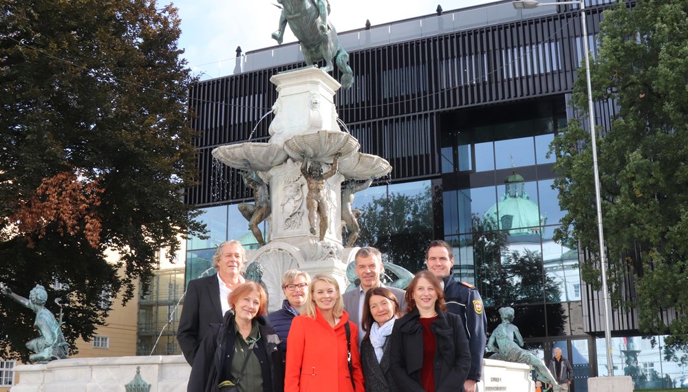 Er ist zurück im Kulturquartier vor dem Haus der Musik Innsbruck (v.l.): Die RestauratorInnen Johannes Schlögl und Elisabeth Krebs, Birgit Neu (Magistratsabteilung V), Stadträtin Elisabeth Mayr, Bürgermeister Georg Willi, Kulturstadträtin Uschi Schwarzl, Direktorin Veronika Sandbichler (Schloss Ambras) und Helmut Hager (Berufsfeuerwehr) hießen das frühbarocke Reiterstandbild Leopolds auf dem gleichnamigen Brunnen willkommen.