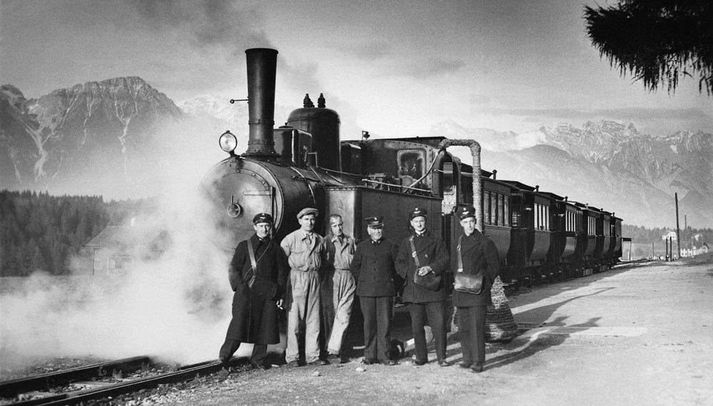 Die Innsbrucker Mittelgebirgsbahn, die „Igler“, mit sechs Waggons in der Station Igls, 1932. Stolz posiert das Straßenbahnpersonal mit Lokomotivführer, Heizer und Schaffner vor der bis 1936 mit Dampf betriebenen Garnitur.