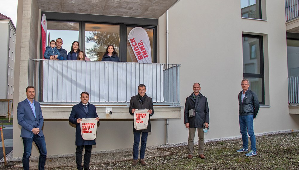 Eine vierköpfige Familie (Balkon, l.) sowie eine weitere Bewohnerin (Balkon, r.) freuen sich gemeinsam mit (vorne, v. l.) IIG-Geschäftsbereichsleiter Bernhard Matt, IIG-Geschäftsführer Franz Danler, Bürgermeister Georg Willi, Martin Franzmair (IIG-Projektleiter) und Nikolaus Reitmeir (IIG-Bauleitung) über ihr neues Zuhause in der Kranewitterstraße.