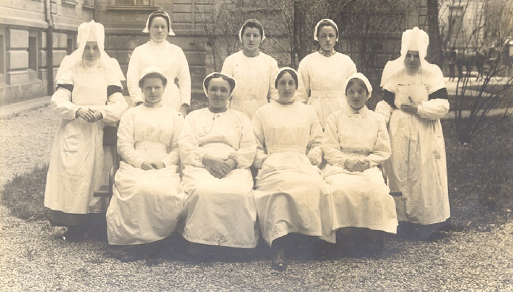 Pflegerinnenkurs im Krankenhaus Innsbruck 1917. Zu sehen sind sieben Krankenpflege-Schülerinnen und zwei Schwestern in Nonnentracht. Aufgenommen im Garten vor einem Pavillon der Klinik.