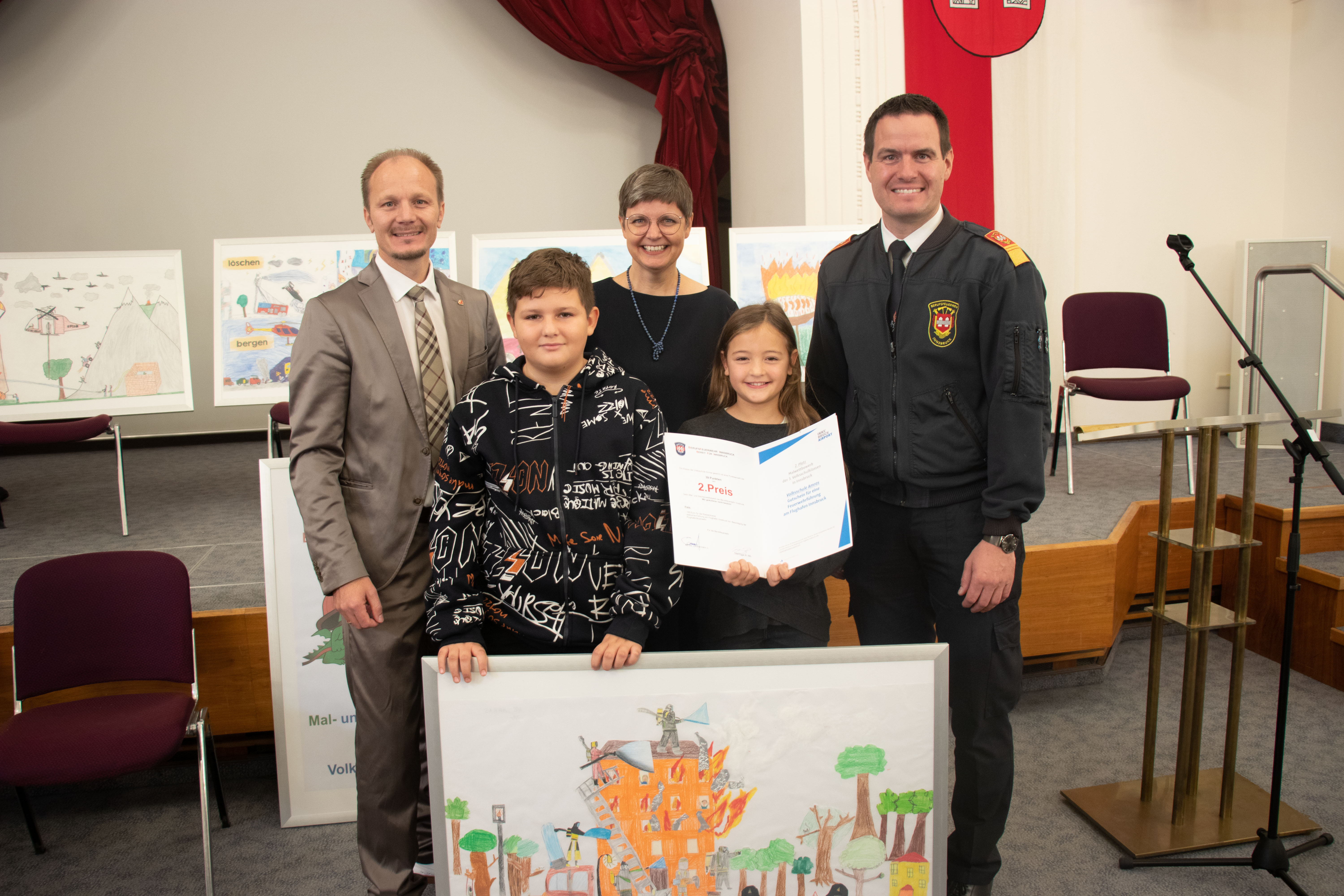 Der zweite Preis geht an die Volksschule Amras, die mit ihrem Bild "Hilfe, es brennt!" die Jury um Vizebürgermeister Johannes Anzengruber (links) und Branddirektor Helmut Hager (rechts) begeistern konnte. 100€ für die Klassenkassa sowie eine Exkursion zum Flughafen und der Flughafenfeuerwehr ist den Kindern sicher.