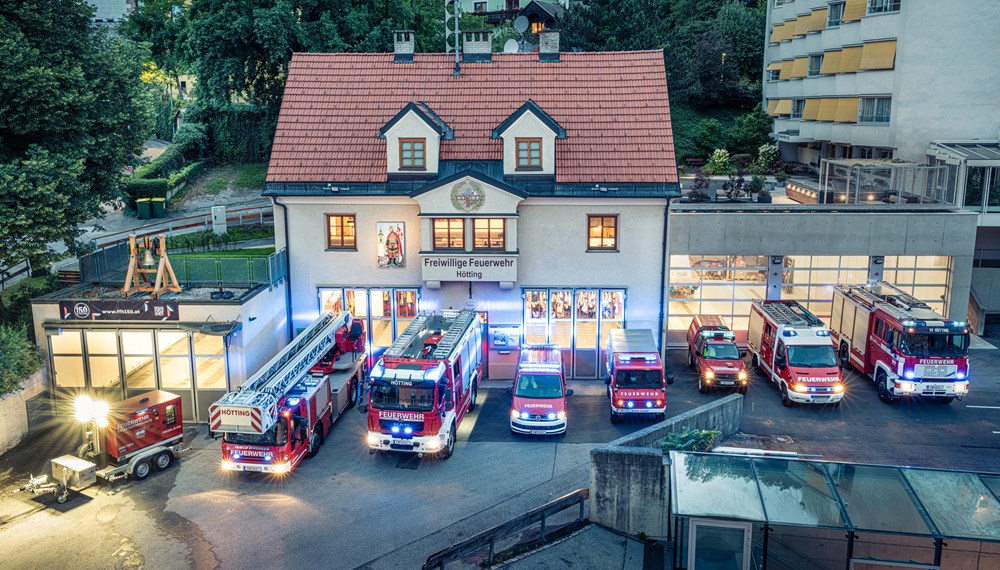 Die Feuerwehr-Wache in Hötting, Schulgasse 6, mit dem renovierten haupthaus von 1929 mittig, die links angebaute Halle von 1975 für die Drehleiter sowie die rechts 2023 neu angebaute Halle - im Vordergrund der derzeitige Fuhrpark.