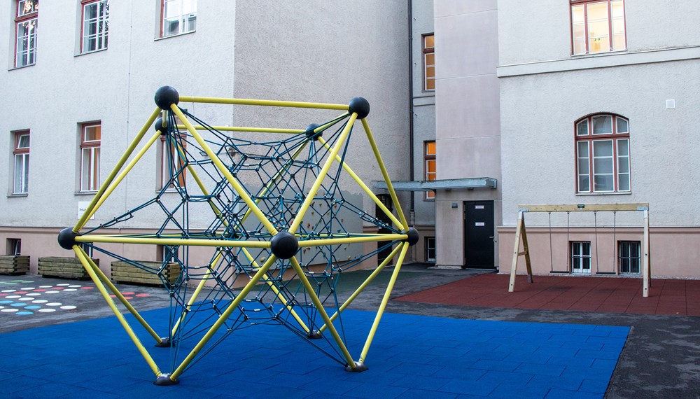 Der Spielbereich im Innenhof konnte ebenfalls saniert werden. Die neue Aufzugsanlage im Hintergrund fügt sich harmonisch in das denkmalgeschützte Umfeld ein und ermöglicht eine barrierefreie Zugänglichkeit.