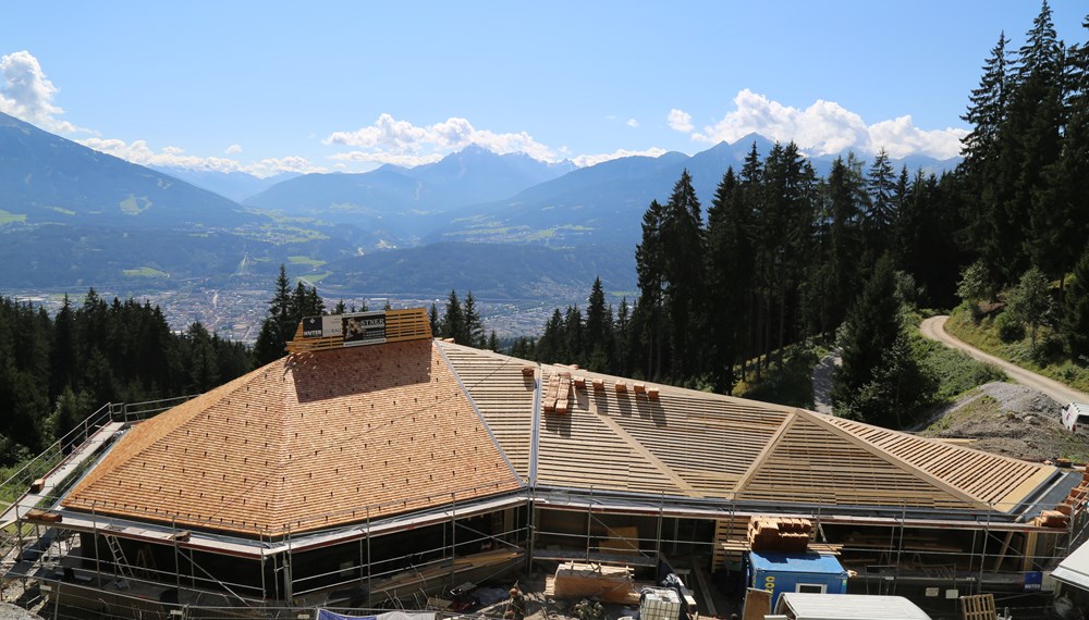 Der Bau der Umbrückler Alm schreitet zügig voran. Das Dach wird aktuell mit Lärchenschindeln eingedeckt und der Estrich wird im Innenraum verlegt. Weiters stehen die Holzwände kurz vor der Errichtung. Zwischenzeitlich kann schon der wunderschöne herbstliche Ausblick über die Tiroler Landeshauptstadt genossen werden.