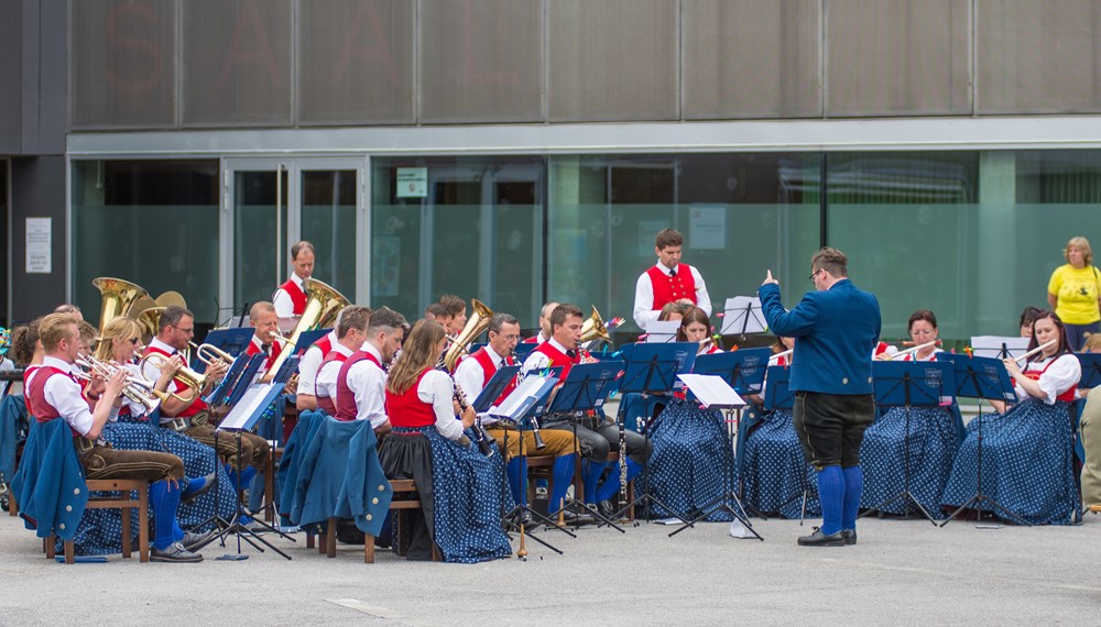 Vizebürgermeister Christoph Kaufmann eröffnete das Platzkonzert der Speckbacher Musikkapelle am DDr. Alois Lugger Platz. Gemeinsam mit der Pfarre St. Pius X und der Freiwilligen Feuerwehr Neu Arzl organisierte die Speckbacher Musikkapelle einen Frühschoppen im Olympischen Dorf .