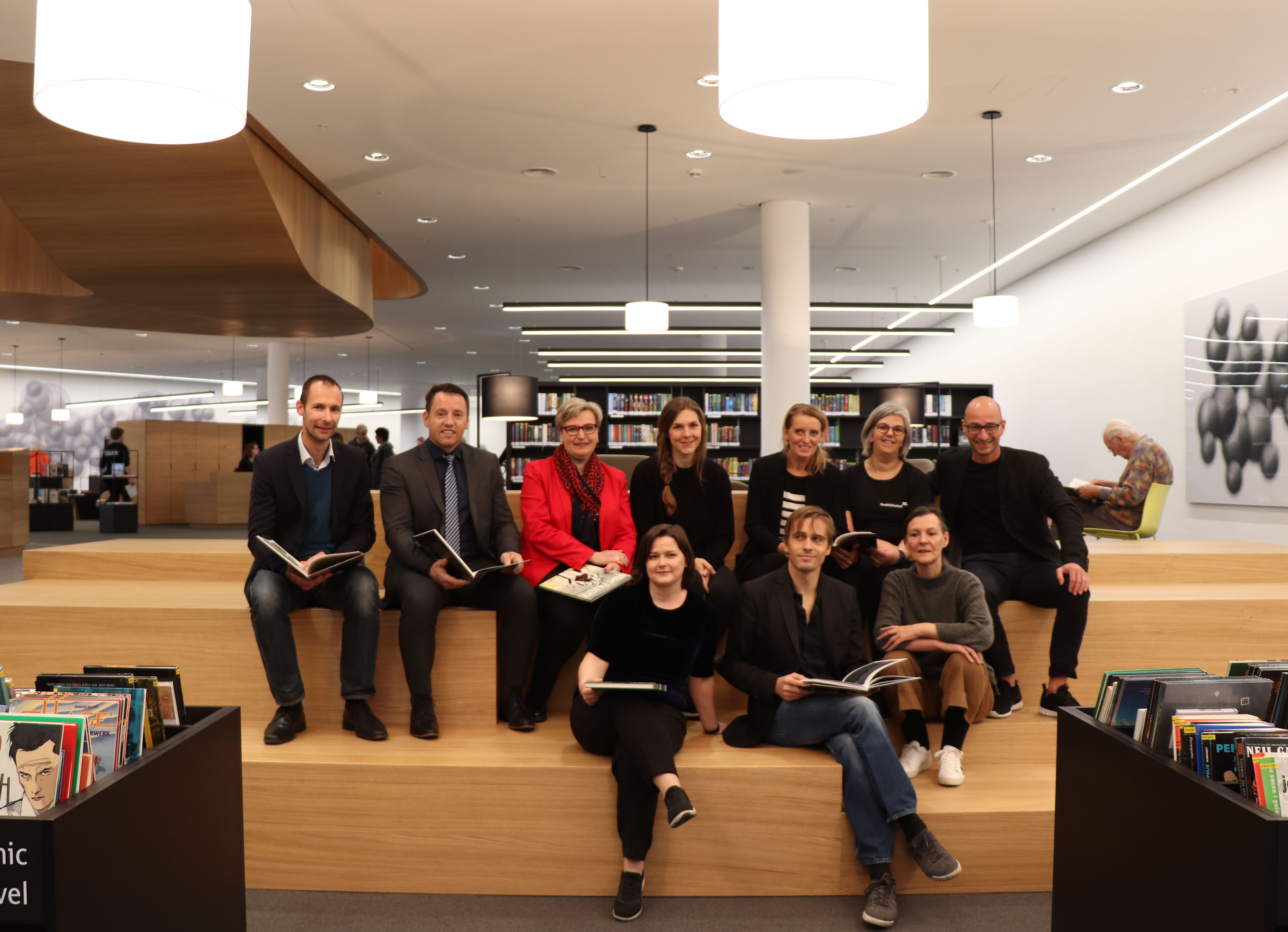 Freuen sich über den neuen Begegnungsort im größten Wohnzimmer der Stadt: Bibliotheksleiterin Christina Krenmayr (2. Reihe, 2. v.r.) und Galerieleiterin Natalie Pedevilla (1. Reihe, li.), Abteilungsleiterin Birgit Neu (2. Reihe, 3. v.l.), Kulturamtsleiterin Maria-Luise Mayr (1. Reihe, re.), Dr. Franz Danler und DI Georg Preyer (beide IIG, 2. Reihe, li.) mit den ArchitektInnen des Architekturbüros LAAC.